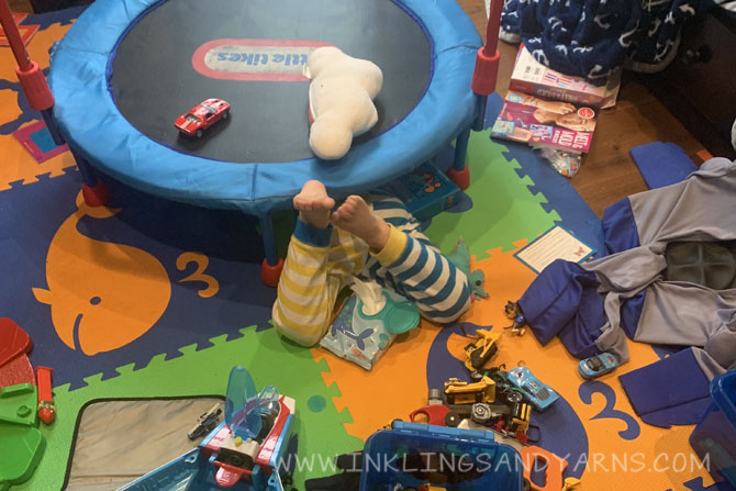 A messy bedroom, with a preschooler's legs sticking out from underneath a small trampoline