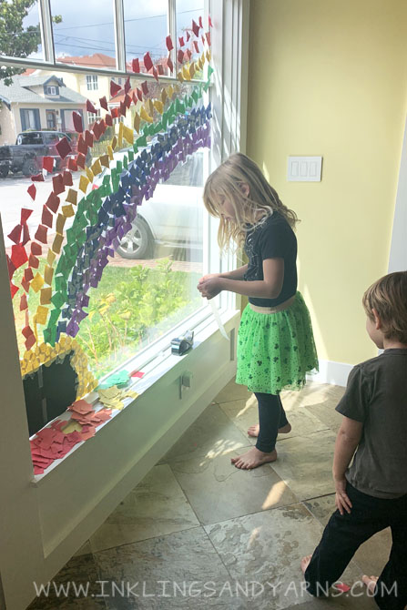 A little boy and little girl making a rainbow collage on their front window.