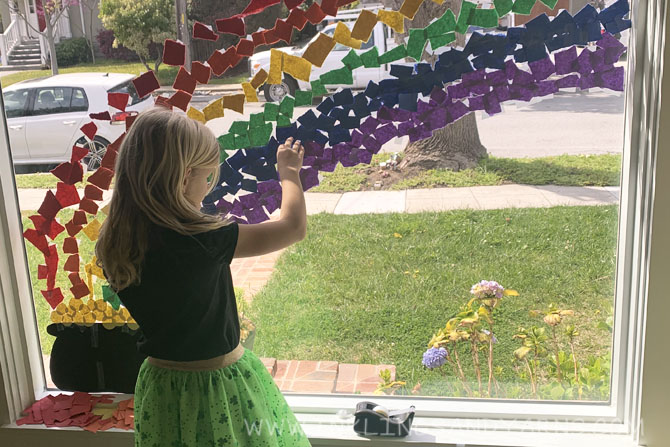 A young girl tapes paper to a window to make a rainbow picture