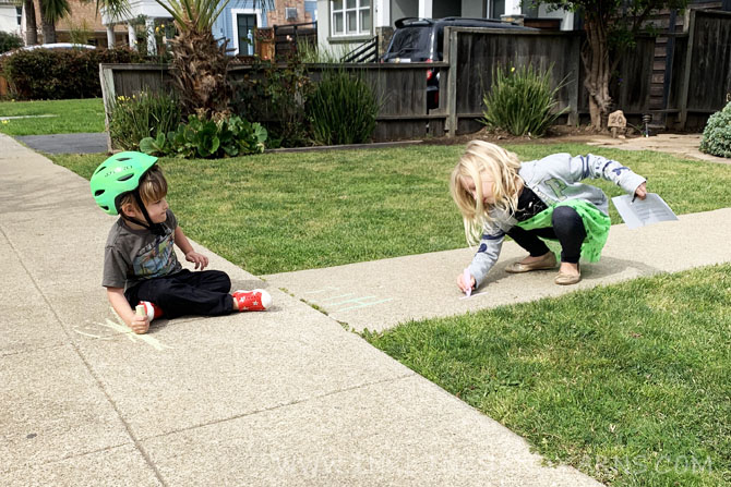 A young boy and girl sitting on the sidewalk, writing messages in chalk.