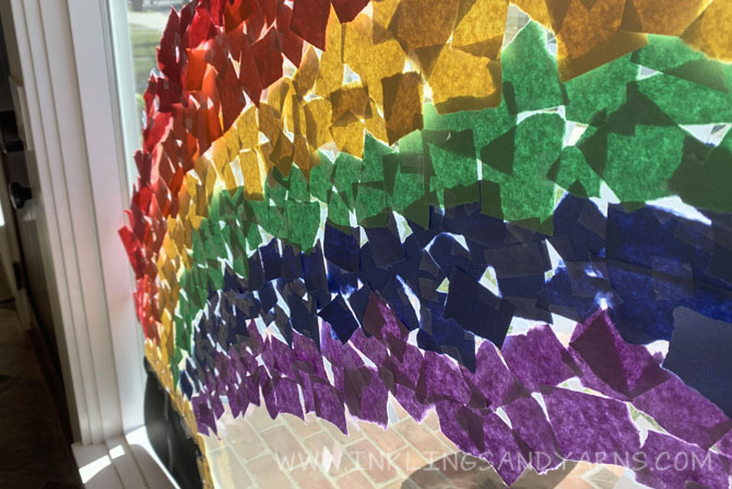 scraps of torn construction paper taped to a window in the shape of a rainbow