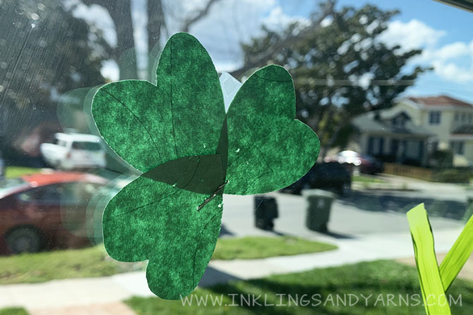 A paper shamrock made by stapling 3 hearts together, taped to a window.